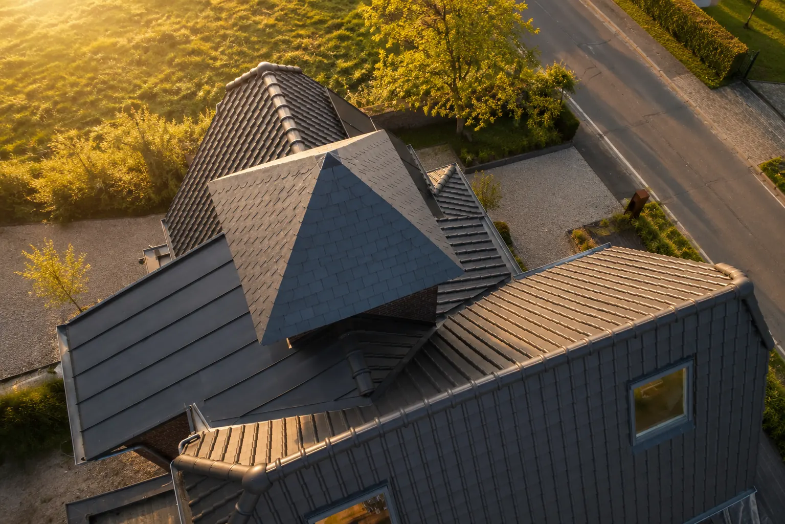 Dronebeeld van complex pannendak met zinkwerk bij gouden uur, openingsbeeld