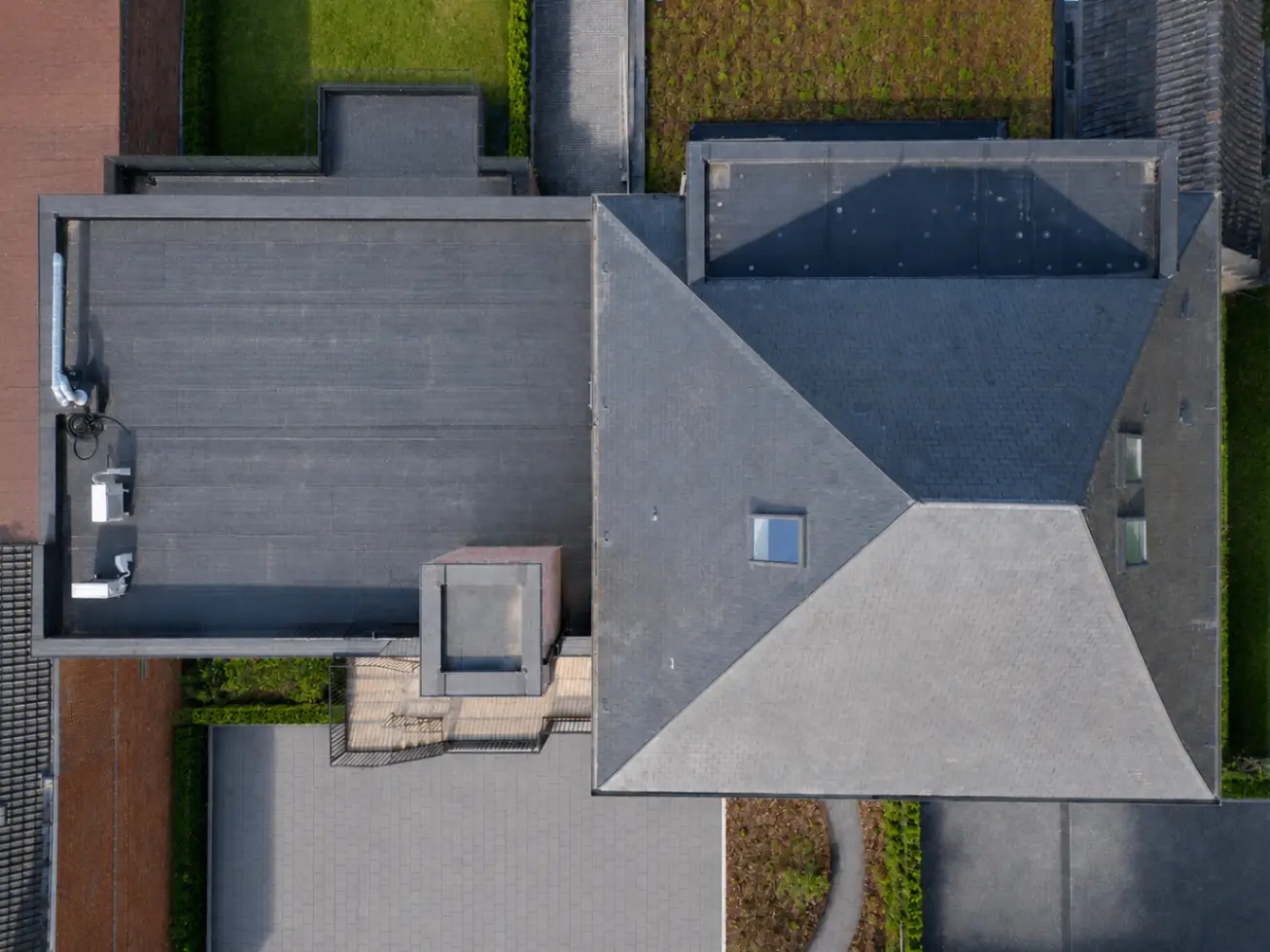 Top-down overzicht van leien piramidedak, platte daken en EPDM-vlakken op De Castel